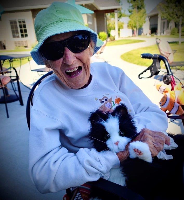 Dolores Gillet, a resident of a care facility, smiles as she holds a robotic cat in her lap.
